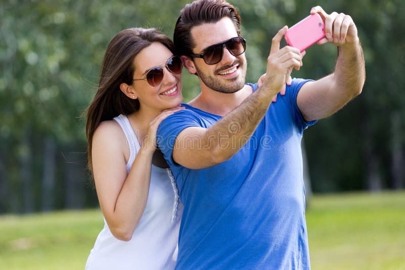 Счастливые молодые пары принимая selfies с ее smartphone в равенстве стоковое изображение rf Счастливые молодые пары принимая selfies с ее smartphone в равенстве стоковое изображение rf