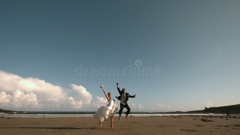 Счастливые пары новобрачных скача в воздух на пляже