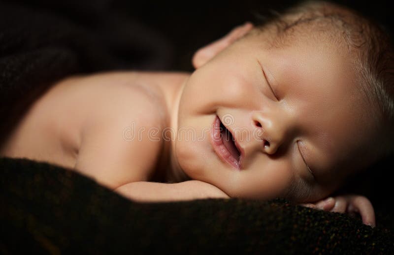 Счастливый newborn младенец усмехаясь в его сне на темноте стоковое изображение rf