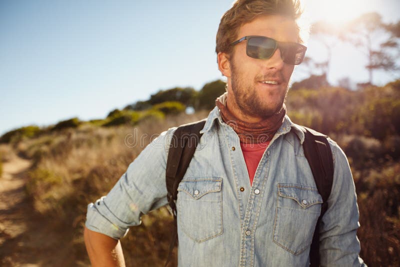 Portrait of happy young man hiking in countryside. Caucasian male model with backpack hiking on sunny day. Summer vacation in countryside. Portrait of happy young man hiking in countryside. Caucasian male model with backpack hiking on sunny day. Summer vacation in countryside.
