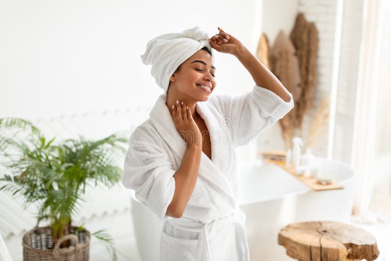 Wellness And Spa. Happy African American Woman Dancing Posing Wearing White Bathrobe Enjoying Beauty Routine After Shower Standing In Modern Bathroom Indoors. Bodycare And Hygiene Concept. Wellness And Spa. Happy African American Woman Dancing Posing Wearing White Bathrobe Enjoying Beauty Routine After Shower Standing In Modern Bathroom Indoors. Bodycare And Hygiene Concept