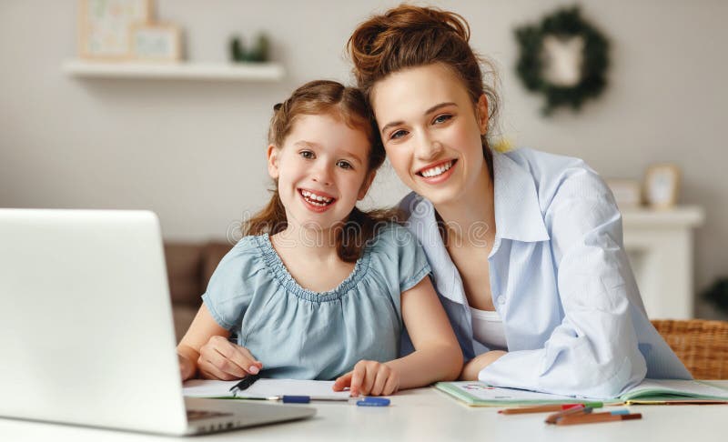 Positive young woman helping daughter in searching information for homework on internet while sitting together at table with laptop at home. Positive young woman helping daughter in searching information for homework on internet while sitting together at table with laptop at home