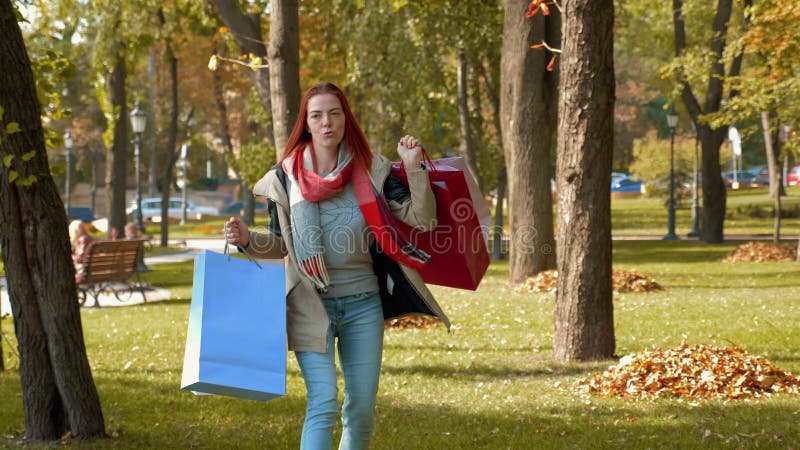 Счастливая девушка с лисиной парикмахерской ходит в парк с покупками в полицветных бумажных сумках и радостями