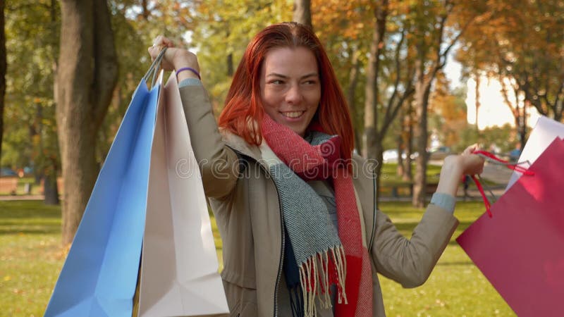 Счастливая девушка с лисиной парикмахерской ходит в парк с покупками в полицветных бумажных сумках и радостями