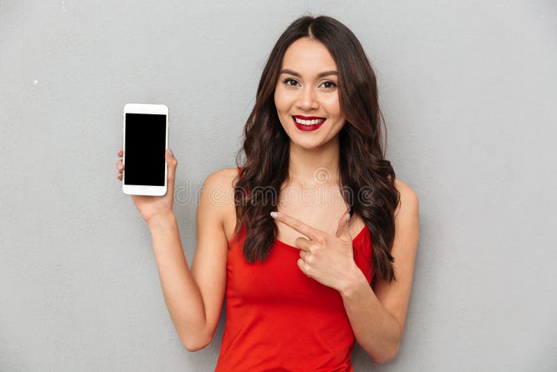 Счастливая женщина брюнет в вскользь одеждах показывая пустой экран smartphone стоковое фото Счастливая женщина брюнет в вскользь одеждах показывая пустой экран smartphone стоковое фото