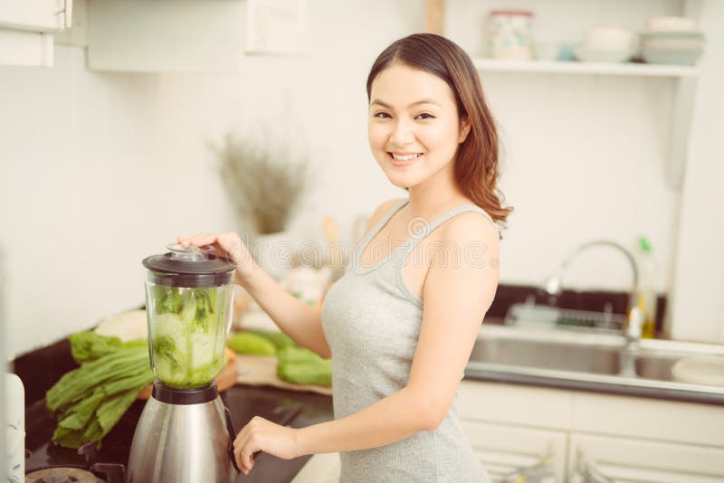 Счастливая женщина смешивая зеленые овощи в blender пока подготавливающ энергичный коктейль стоковое изображение Счастливая женщина смешивая зеленые овощи в blender пока подготавливающ энергичный коктейль стоковое изображение