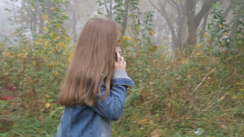 Счастливая красивая девушка идя лесом и говоря сотовым телефоном