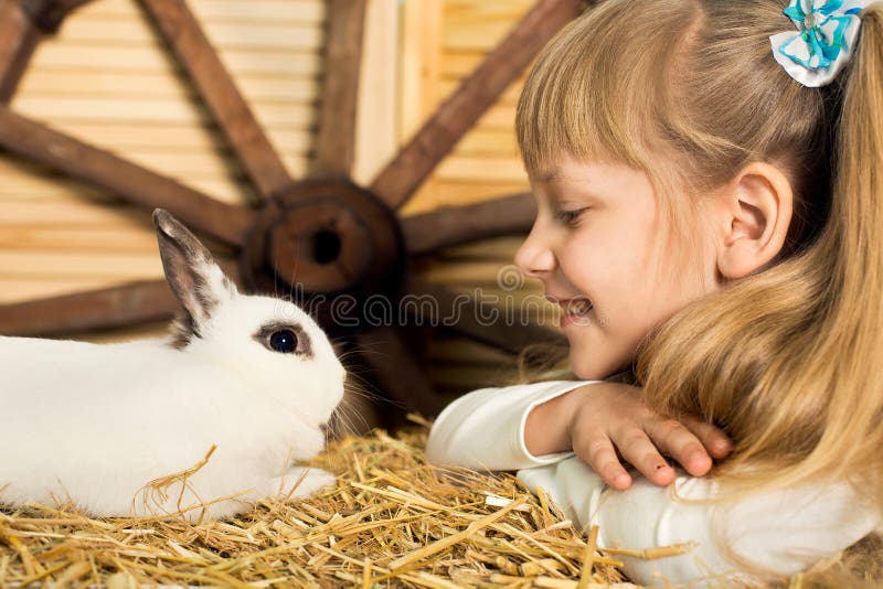 счастливая маленькая девочка в платье сидит в гнезде и держит миленького белого пасхального кролика