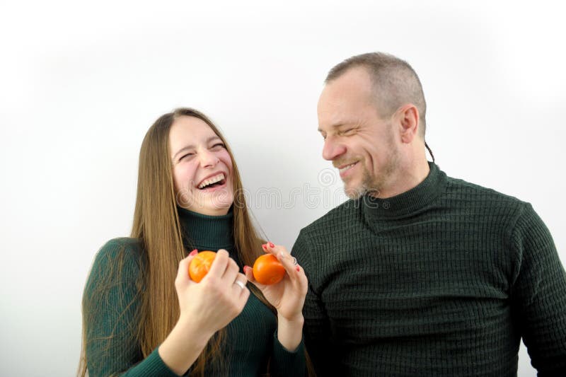 Happy laughing couple kissing talking and peeling tangerines. Pregnant Caucasian wife and smiling husband enjoying Christmas celebration at home indoors. Happy laughing couple kissing talking and peeling tangerines. Pregnant Caucasian wife and smiling husband enjoying Christmas celebration at home indoors.