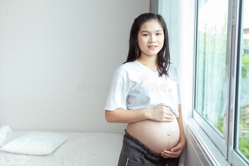 Счастливая тайская беременная женщина с большим tummy ослабляет дома Портрет беременного зрелого положения женщины около окна и л стоковая фотография rf Счастливая тайская беременная женщина с большим tummy ослабляет дома Портрет беременного зрелого положения женщины около окна и л стоковая фотография rf