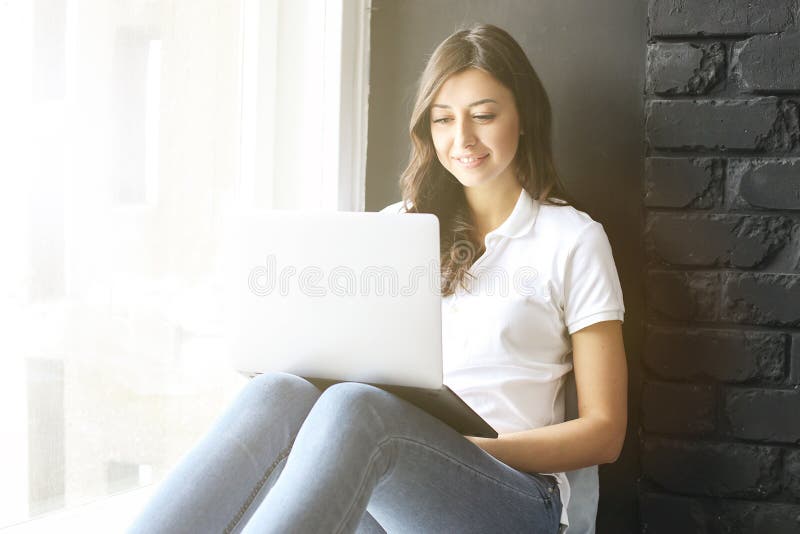 Счастливая тысячелетняя девушка с компьтер-книжкой на windowsill Портрет молодой женщины с зазором diastema между зубами красивей стоковые фотографии rf Счастливая тысячелетняя девушка с компьтер-книжкой на windowsill Портрет молодой женщины с зазором diastema между зубами красивей стоковые фотографии rf
