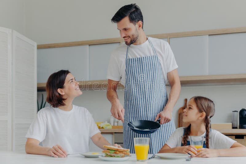 Счастливые мать и дочь отца собираются вместе на кухне есть очень вкусный завтрак папы подготовили яичница, оказаться в хорошем на стоковая фотография
