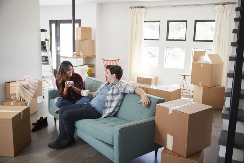 Счастливые пары отдыхая на софе окруженной коробками в новом доме на Moving день стоковое изображение Счастливые пары отдыхая на софе окруженной коробками в новом доме на Moving день стоковое изображение