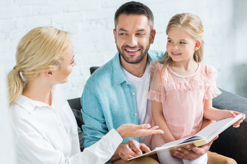 счастливые родители с милой маленькой книгой чтения дочери совместно стоковые изображения