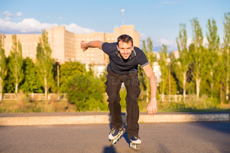 Счастливый молодой человек rollerblading в парке города на заходе солнца стоковое фото rf Счастливый молодой человек rollerblading в парке города на заходе солнца стоковое фото rf