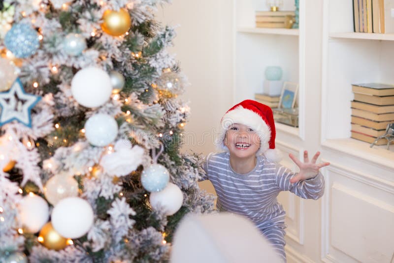 счастливый новый год xmas Счастливый усмехаясь мальчик во взгляде Санта красном удивительно из рождественской елки крыто Рождеств стоковое изображение счастливый новый год xmas Счастливый усмехаясь мальчик во взгляде Санта красном удивительно из рождественской елки крыто Рождеств стоковое изображение