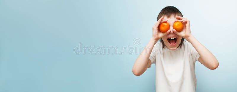 счастливый улыбающийся мальчик с двумя мандаринами, закрывающими глаза на синий фон стоковое фото rf