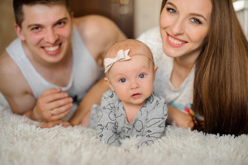 Счастливый усмехаться parents лежать на кровати с милым newborn ребёнком стоковое изображение rf Счастливый усмехаться parents лежать на кровати с милым newborn ребёнком стоковое изображение rf