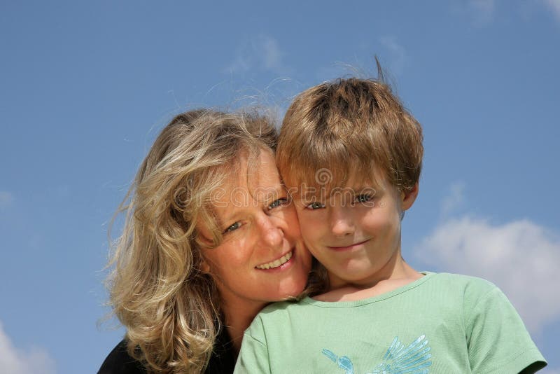 A beautiful mother with her 7-years old son, both smiling, photographed in the summer sun with blue sky and clouds in the background. A beautiful mother with her 7-years old son, both smiling, photographed in the summer sun with blue sky and clouds in the background