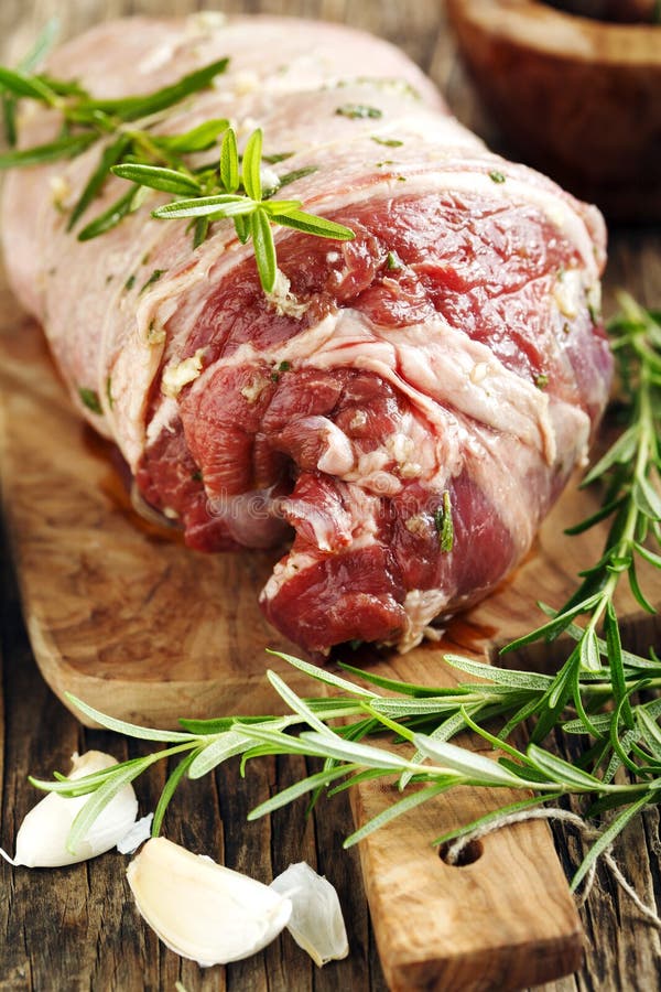 Raw boneless lamb leg with garlic and rosemary on wooden cooking board. Raw boneless lamb leg with garlic and rosemary on wooden cooking board