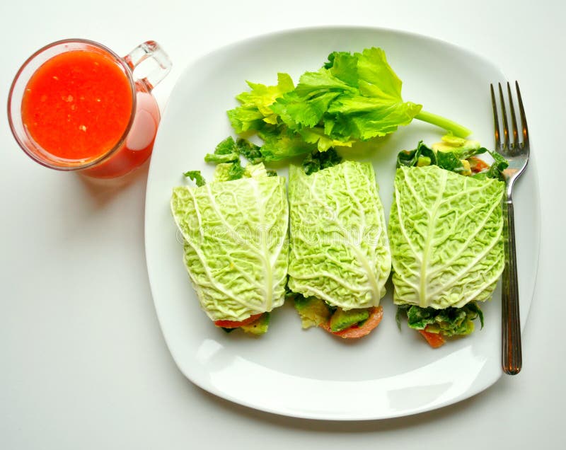 Raw food diet concept with cabbage wraps filled with tomato , spinach and avocado and red orange juice . vegan dish with fresh vegetables. detox, detoxification diet. Raw food diet concept with cabbage wraps filled with tomato , spinach and avocado and red orange juice . vegan dish with fresh vegetables. detox, detoxification diet.