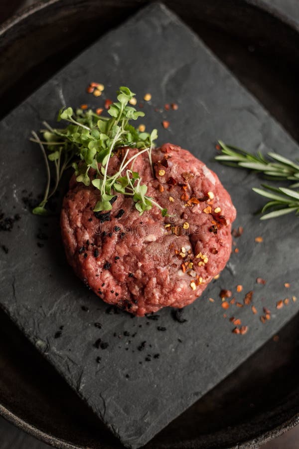 Сырцовые котлеты стейка мяса говяжего фарша с травами и специями на черной доске Ресторан стоковые фотографии rf Сырцовые котлеты стейка мяса говяжего фарша с травами и специями на черной доске Ресторан стоковые фотографии rf