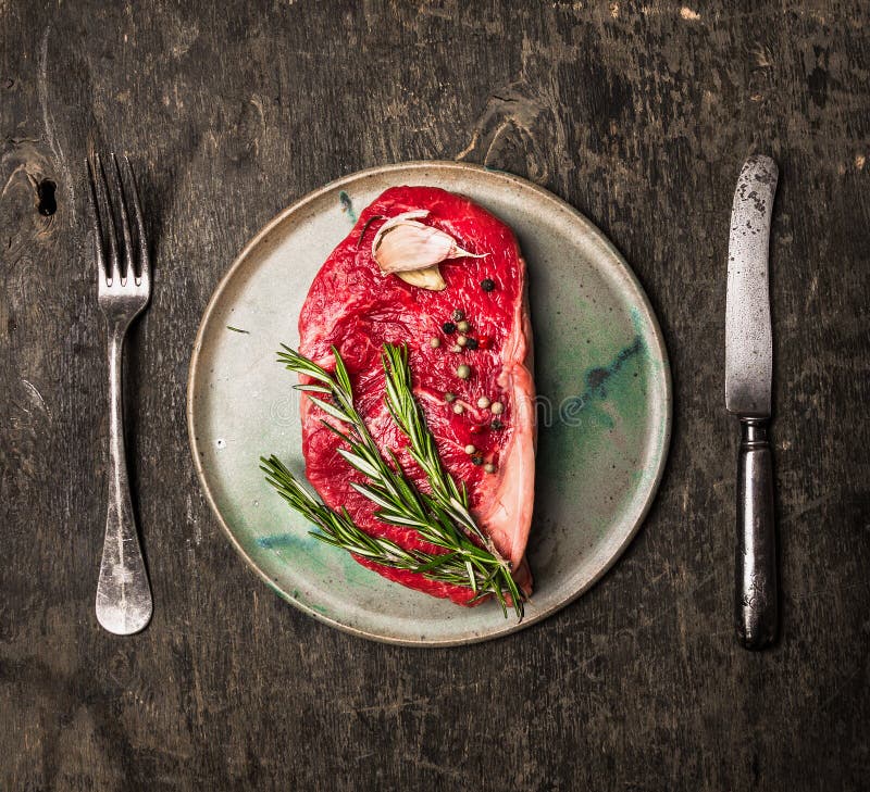 Сырцовый стейк Striploin на плите с розмариновым маслом, чесноком, солью и перцем на темной деревянной предпосылке стоковые фото Сырцовый стейк Striploin на плите с розмариновым маслом, чесноком, солью и перцем на темной деревянной предпосылке стоковые фото
