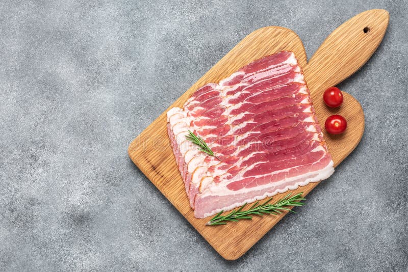 сырые куриные ломтики бекона на деревянной доске с розмарином и томатом. серый фон. плоская копия представления сверху стоковое изображение