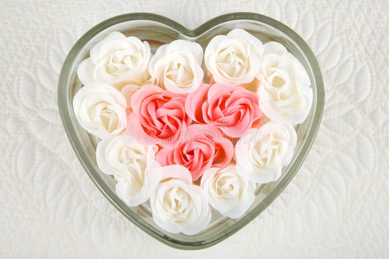 Close uo of beautiful pink and ivory roses fill heart-shaped dish against a quilted background. Close uo of beautiful pink and ivory roses fill heart-shaped dish against a quilted background.