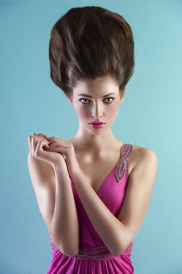 Very elegant young pretty wearing a pink long dress with creative hair style over light turquoise background. Very elegant young pretty wearing a pink long dress with creative hair style over light turquoise background