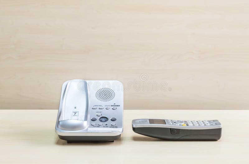 Gray phone , office phone on blurred wooden desk and wall textured background in the meeting room under window light. Gray phone , office phone on blurred wooden desk and wall textured background in the meeting room under window light