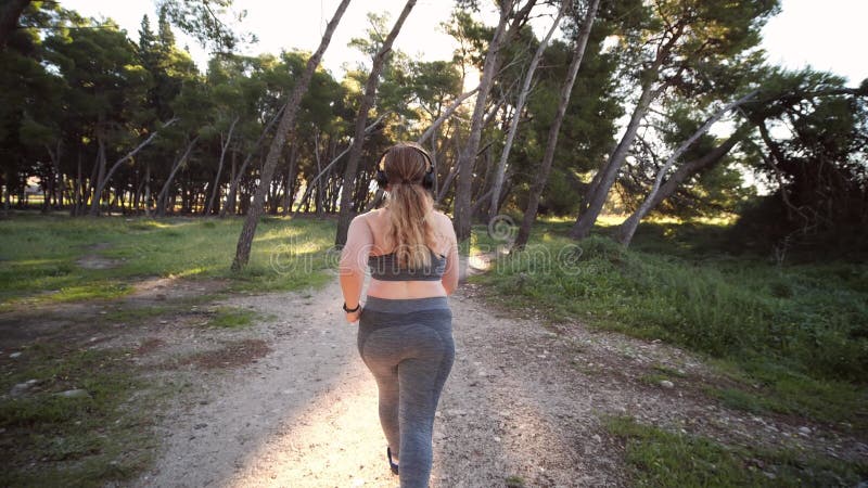 телопозитивная плюс женская спортсменка, бегающая в солнечном парке. концепция потери веса и активный образ жизни