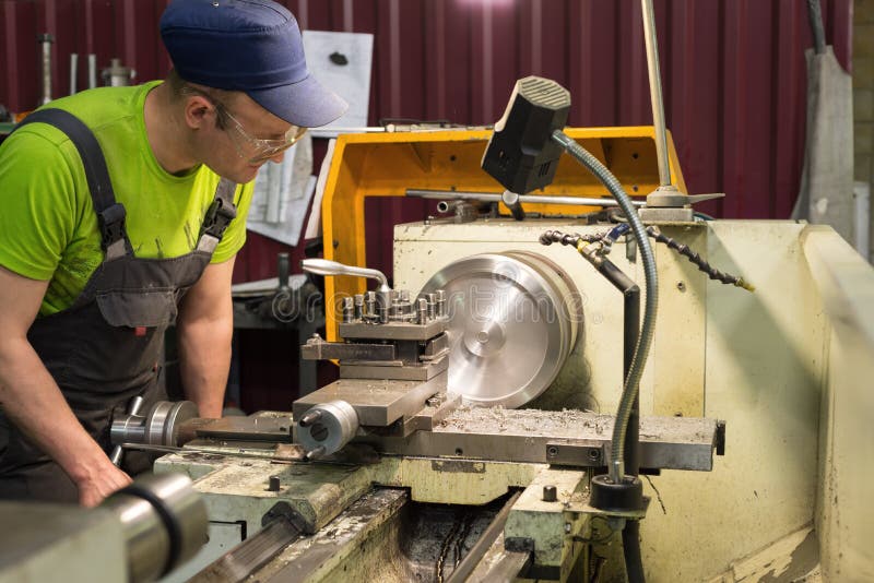 Тернер детенышей обрабатывает workpiece металла на механически токарном станке стоковое изображение rf Тернер детенышей обрабатывает workpiece металла на механически токарном станке стоковое изображение rf