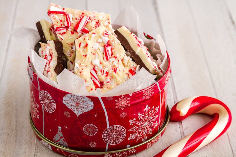 Homemade chocolate peppermint bark in decorative tin with candy cane. Homemade chocolate peppermint bark in decorative tin with candy cane