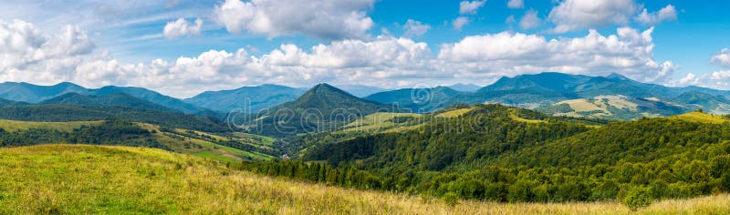 Panorama of a beautiful landscape. grassy meadows and forested hills in early autumn. mountain ridge in the distance beneath a blue sky with clouds. Panorama of a beautiful landscape. grassy meadows and forested hills in early autumn. mountain ridge in the distance beneath a blue sky with clouds