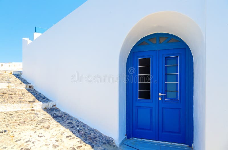 Традиционный белый греческий фасад дома с голубой дверью Santorini, Грецией стоковая фотография rf Традиционный белый греческий фасад дома с голубой дверью Santorini, Грецией стоковая фотография rf