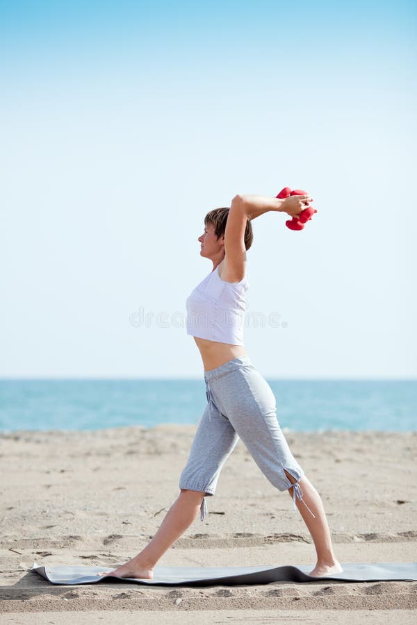 Woman doing exercise with dumbell on beach. Woman doing exercise with dumbell on beach