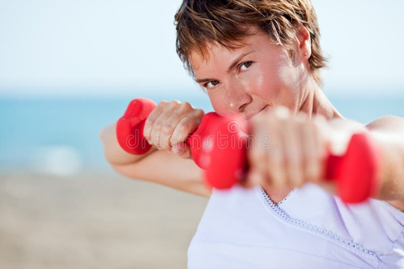 Woman doing exercise with dumbell on beach. Woman doing exercise with dumbell on beach