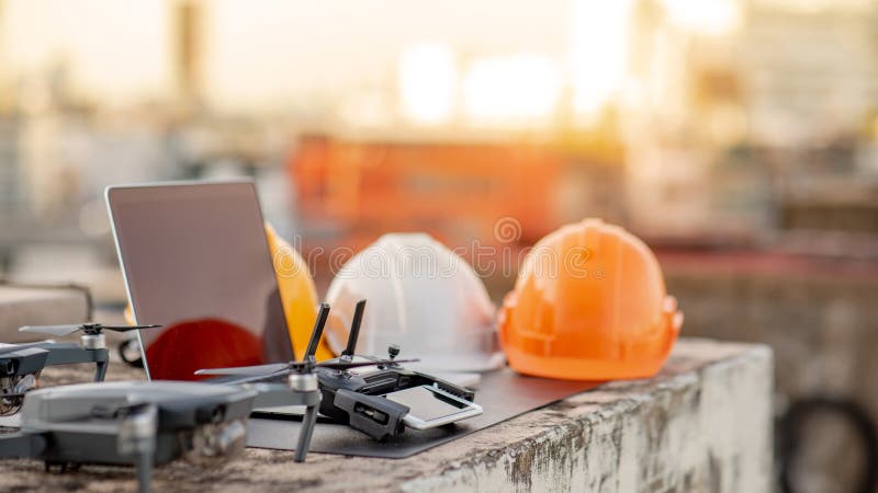 Drone, remote control, smartphone, laptop computer and protective helmet at construction site. Using unmanned aerial vehicle UAV for land and building site survey in civil engineering project. Drone, remote control, smartphone, laptop computer and protective helmet at construction site. Using unmanned aerial vehicle UAV for land and building site survey in civil engineering project.