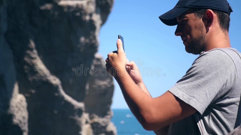 Турист в крышке делает фото из красивой скалы около моря HD, 1920x1080 движение медленное