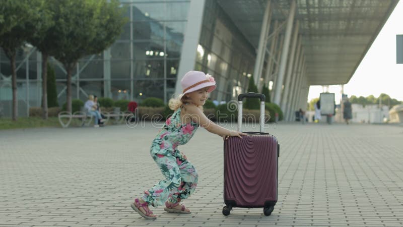 Турист девушки ребенка с сумкой чемодана, недалеко от аэропорта. Небольшой скачок танца ребенок отпраздновать с багажом видеоматериал