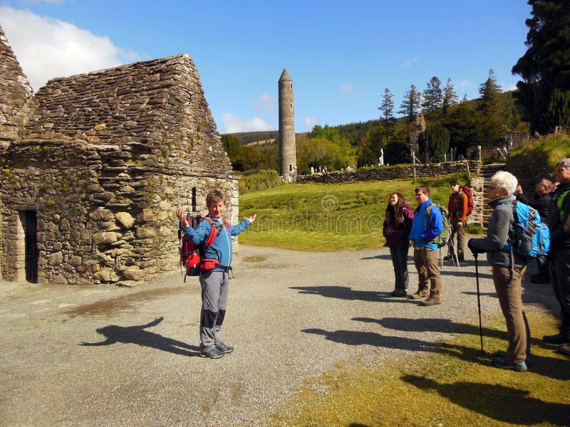 An Irish archeologist conducts a guided history tour of an early medieval monastic settlement in Glendalough located in County Wicklow, Ireland. Behind him are the stone ruins of St. Kevinâ€™s Church also known as â€œKitchenâ€. In the background can be seen an ancient round tower and cemetery. An Irish archeologist conducts a guided history tour of an early medieval monastic settlement in Glendalough located in County Wicklow, Ireland. Behind him are the stone ruins of St. Kevinâ€™s Church also known as â€œKitchenâ€. In the background can be seen an ancient round tower and cemetery.