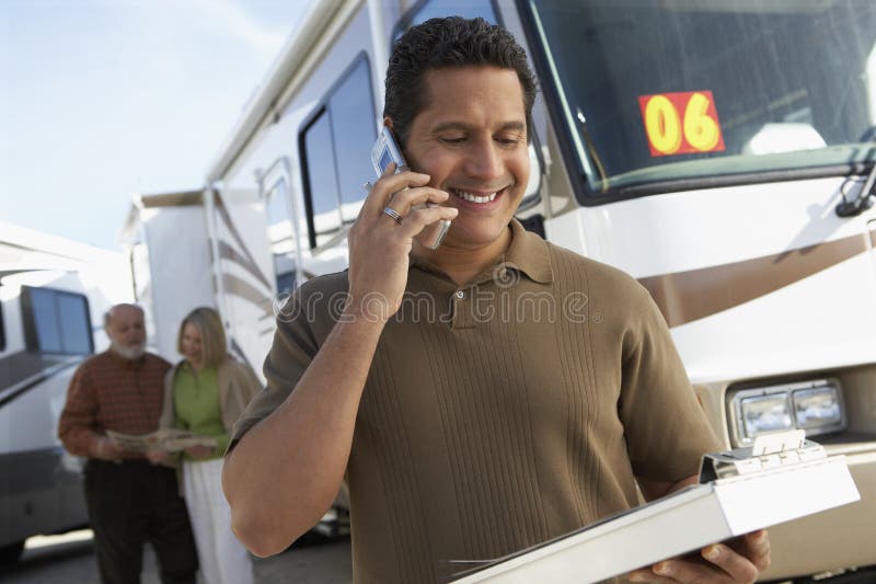 Mature tourist guide talking on phone while holding a book with passengers in background. Mature tourist guide talking on phone while holding a book with passengers in background