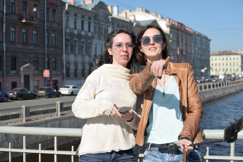Туристы молодых дам в selfies взятия Санкт-Петербурга России на деревянном мосте в историческом центре города стоковые фотографии rf Туристы молодых дам в selfies взятия Санкт-Петербурга России на деревянном мосте в историческом центре города стоковые фотографии rf