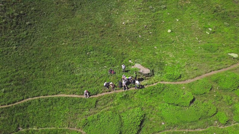 Туристы, сидя на зеленой траве, горы. Клип. Вид сверху группы туристов отдыхает на игру в предгорьях