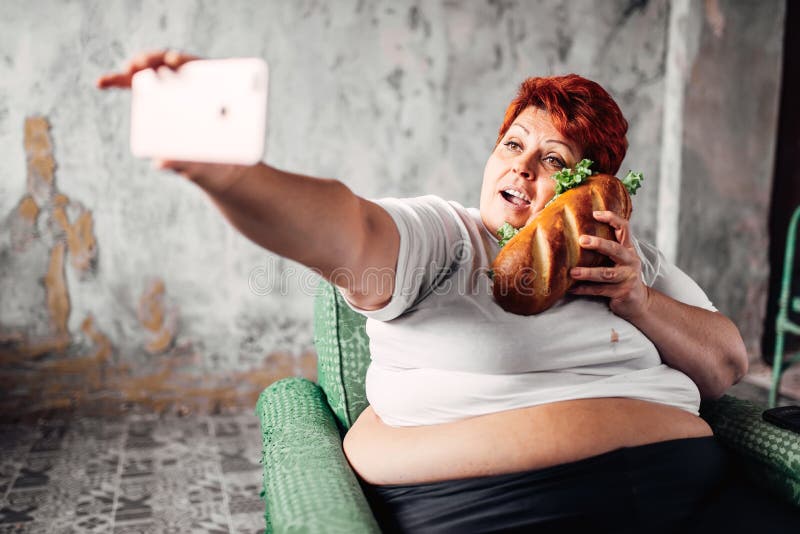 Тучная женщина с сандвичем в руке делает selfie стоковая фотография Тучная женщина с сандвичем в руке делает selfie стоковая фотография
