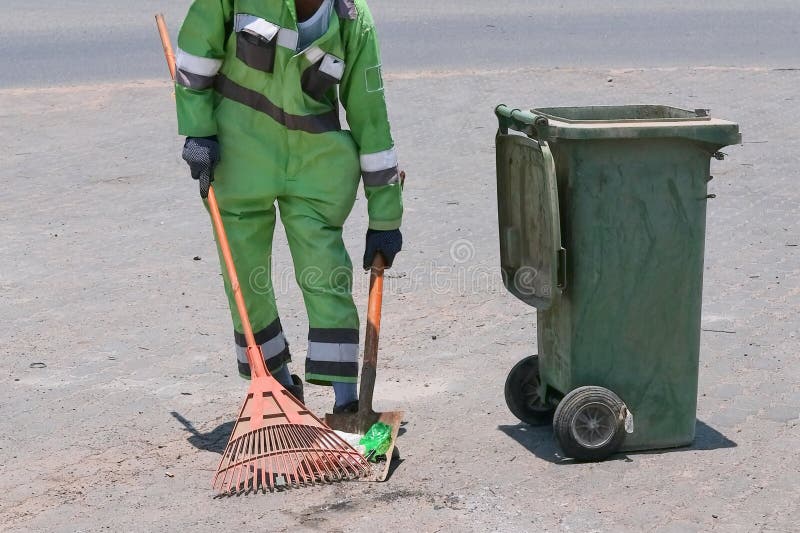 Street cleaning, male municipal worker in fluorescent uniform collecting street rubbish to dumpster. Labor law, labor rights  for migrants, refugee, unskilled labor. Street cleaning, male municipal worker in fluorescent uniform collecting street rubbish to dumpster. Labor law, labor rights  for migrants, refugee, unskilled labor