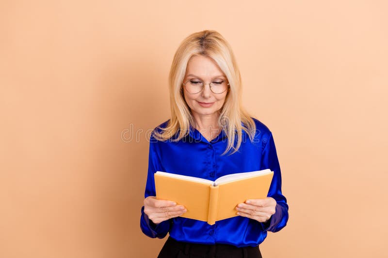 Уверенная зрелая женщина читает книгу в деловом одеянии на бежевом фоне, символизирующем знания и стоковое фото