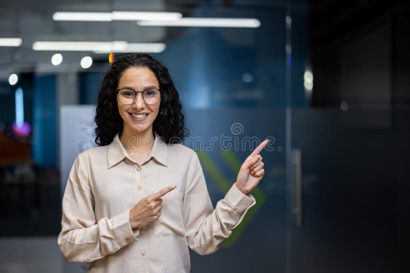 A professional businesswoman with curly hair smiles and points beside her in a modern office setting, exuding confidence and positivity. A professional businesswoman with curly hair smiles and points beside her in a modern office setting, exuding confidence and positivity.