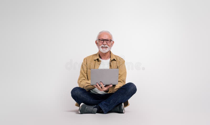 Confident senior male professional checking e-mails over laptop while sitting on white background. Confident senior male professional checking e-mails over laptop while sitting on white background.